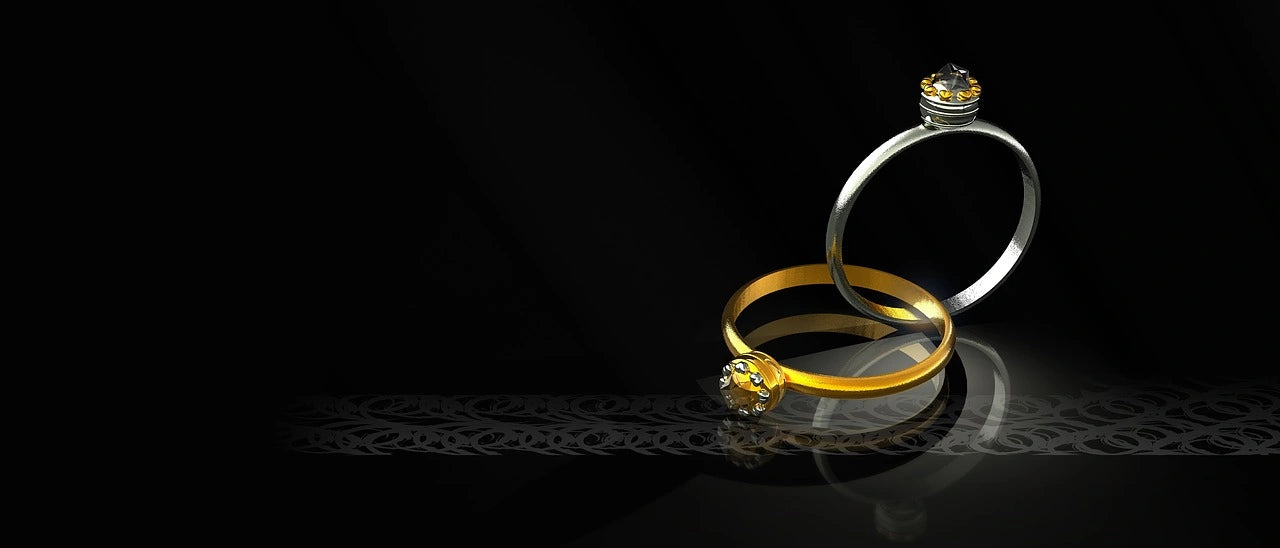 Two gold and diamond engagement rings are placed in a darkest background