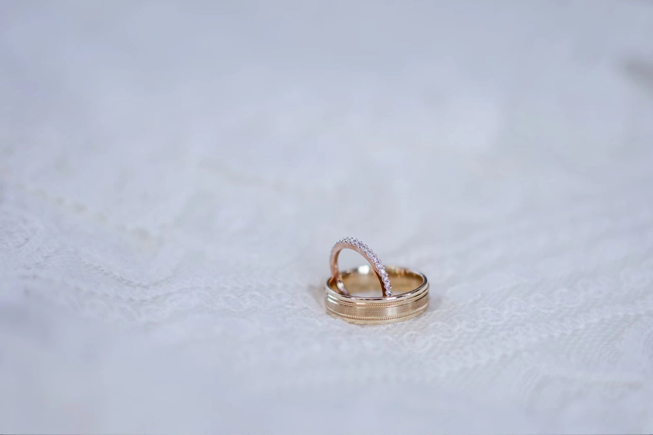 Two gold colored engagement rings placed on white bedsheet