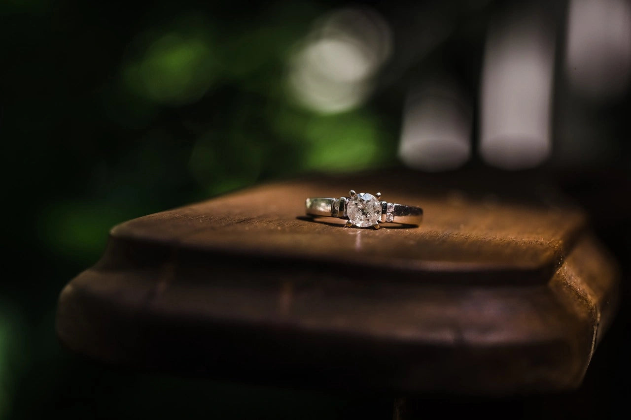Diamond engagement ring placed on a wooden surface in a dark background