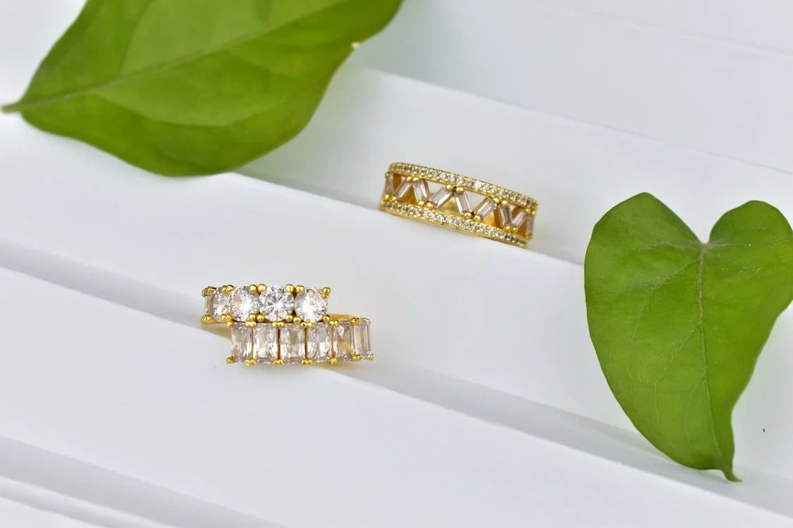 gold rings with gem placed on a white steps besides the leaf