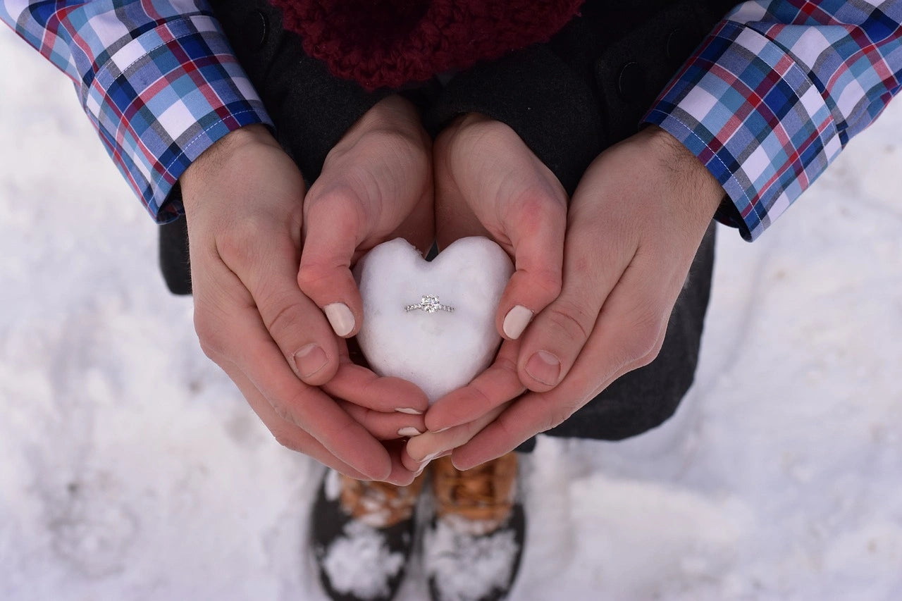 a couple clasps hands in a snowfall, adorned by the gleam of an engagement ring