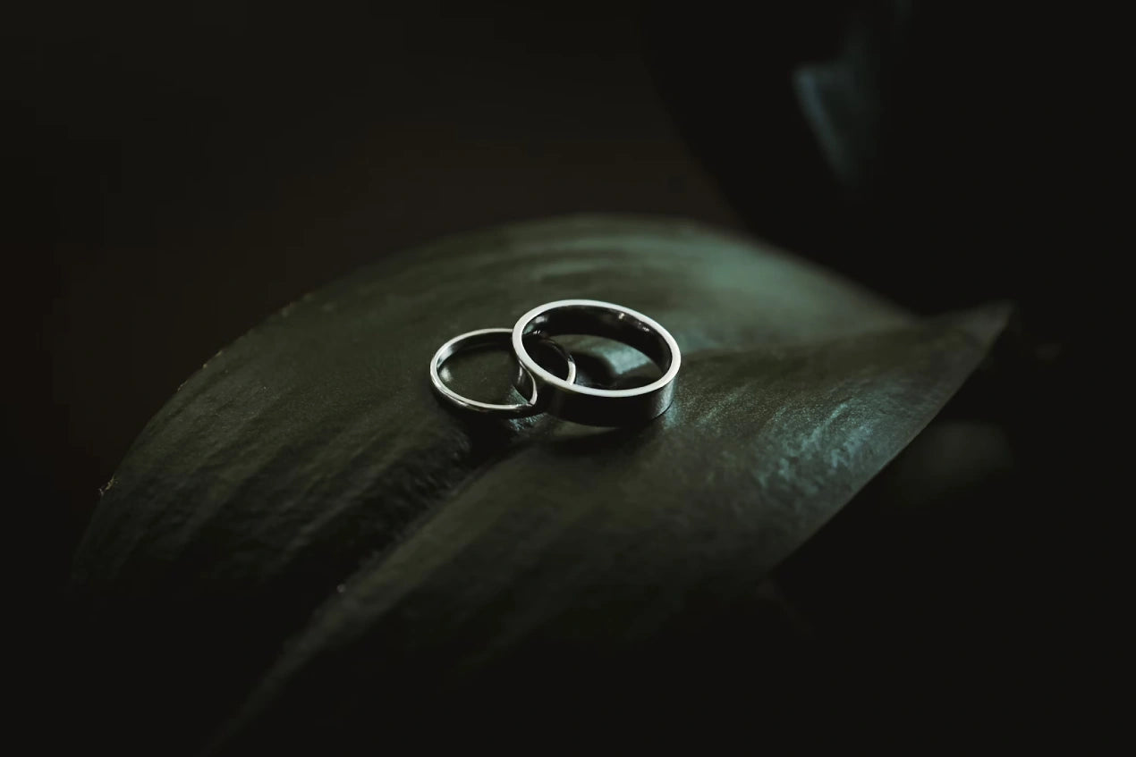 Two silver colored engagement rings placed on the leaf with dark background