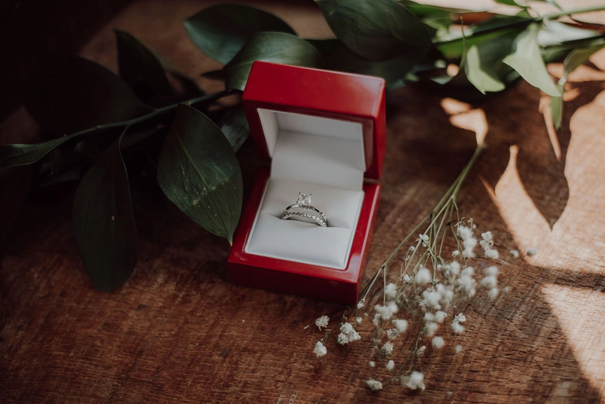 An engagement ring unveiled in an open box, adorning a table adorned with delicate flowers and leaves, a scene of nature's elegance framing the promise within