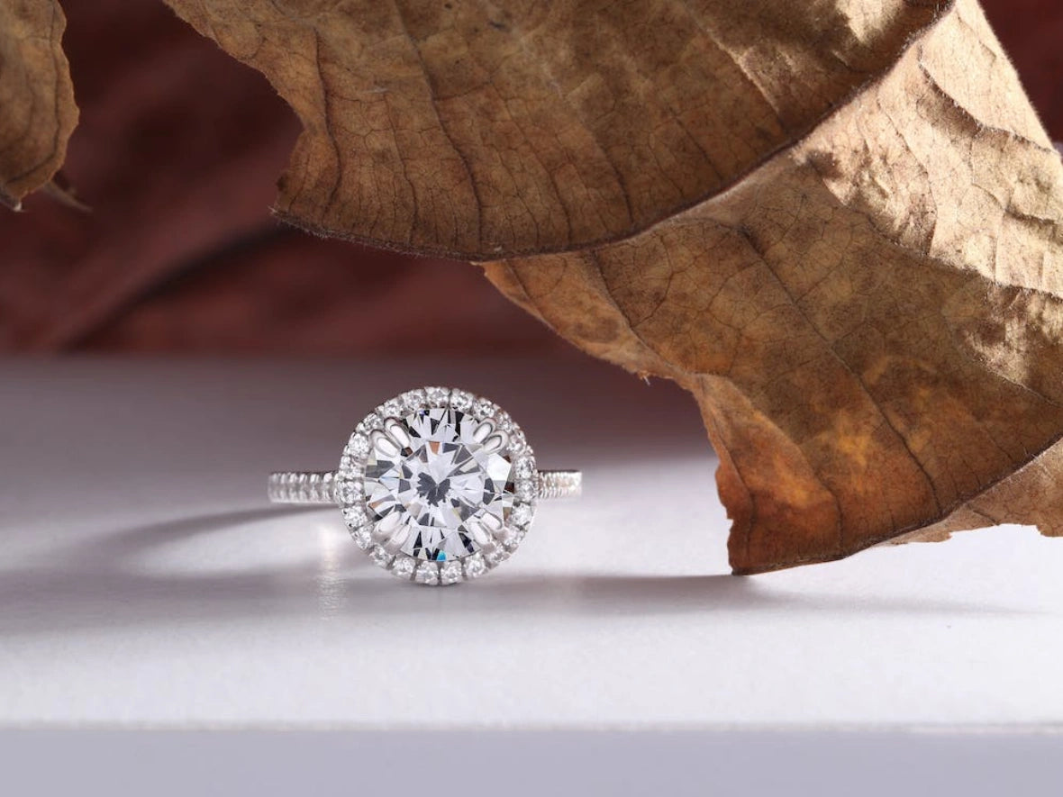 A diamond ring on the white table top with dry leaf