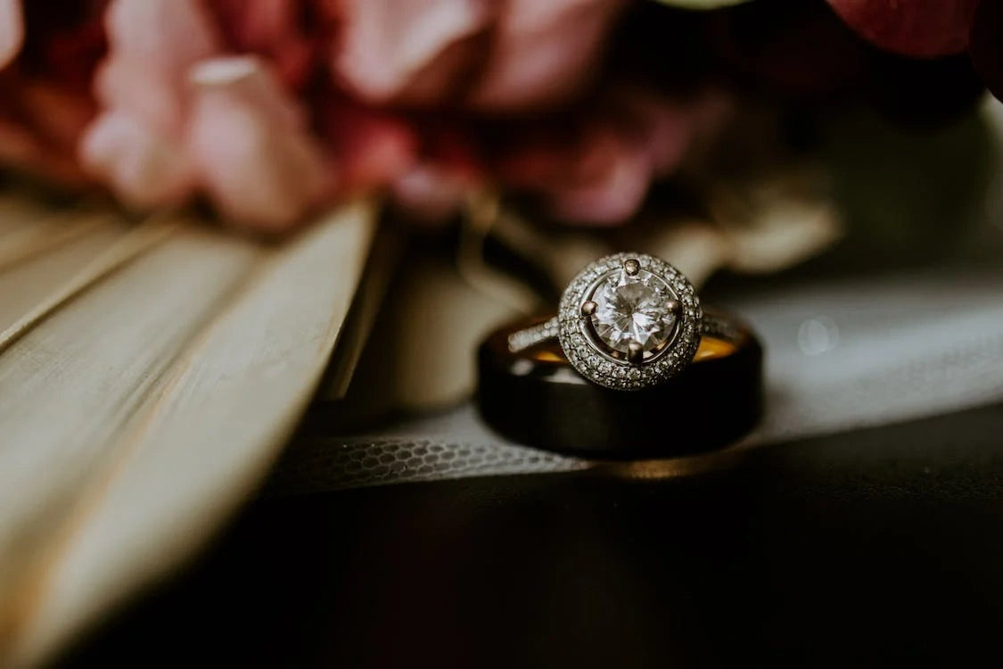 A beautiful silver colored engagement ring on a table with some flowers