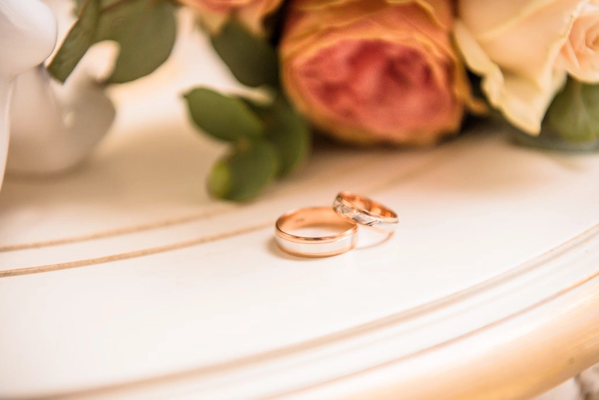 Two Goldish  Engagement rings places on a table with some roses