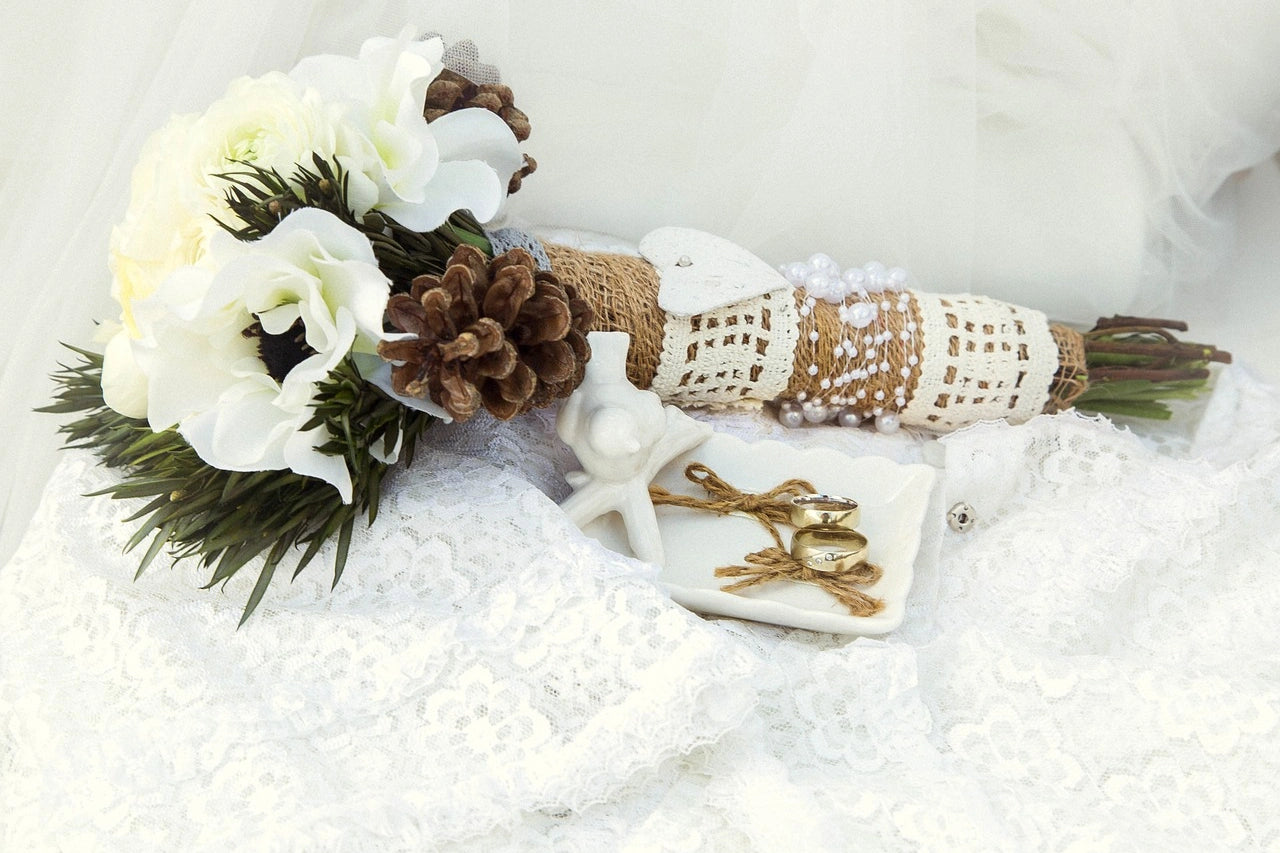 Engagement rings are placed on a white cloth beside the white flower bouquet