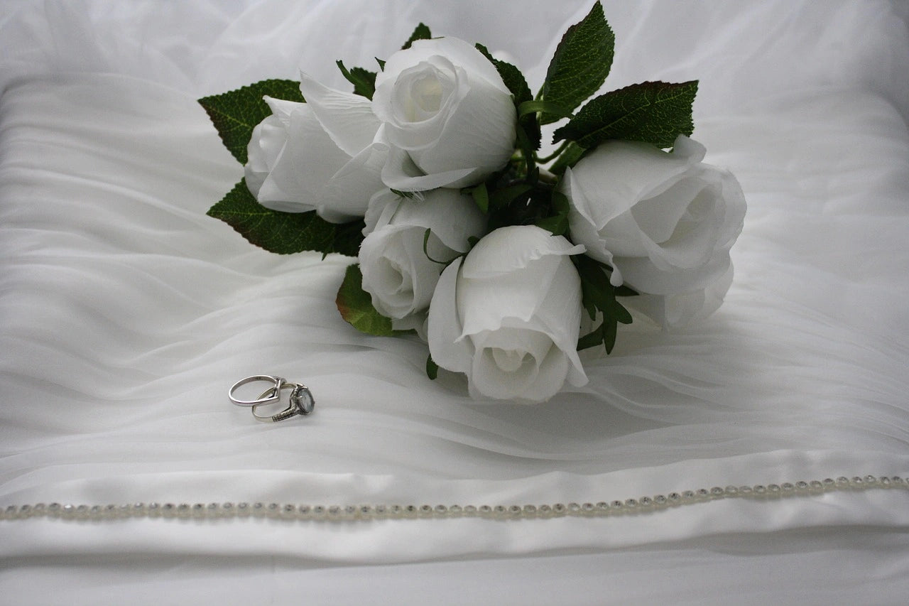Engagement rings placed on a white blanket besides the white flower bouquet