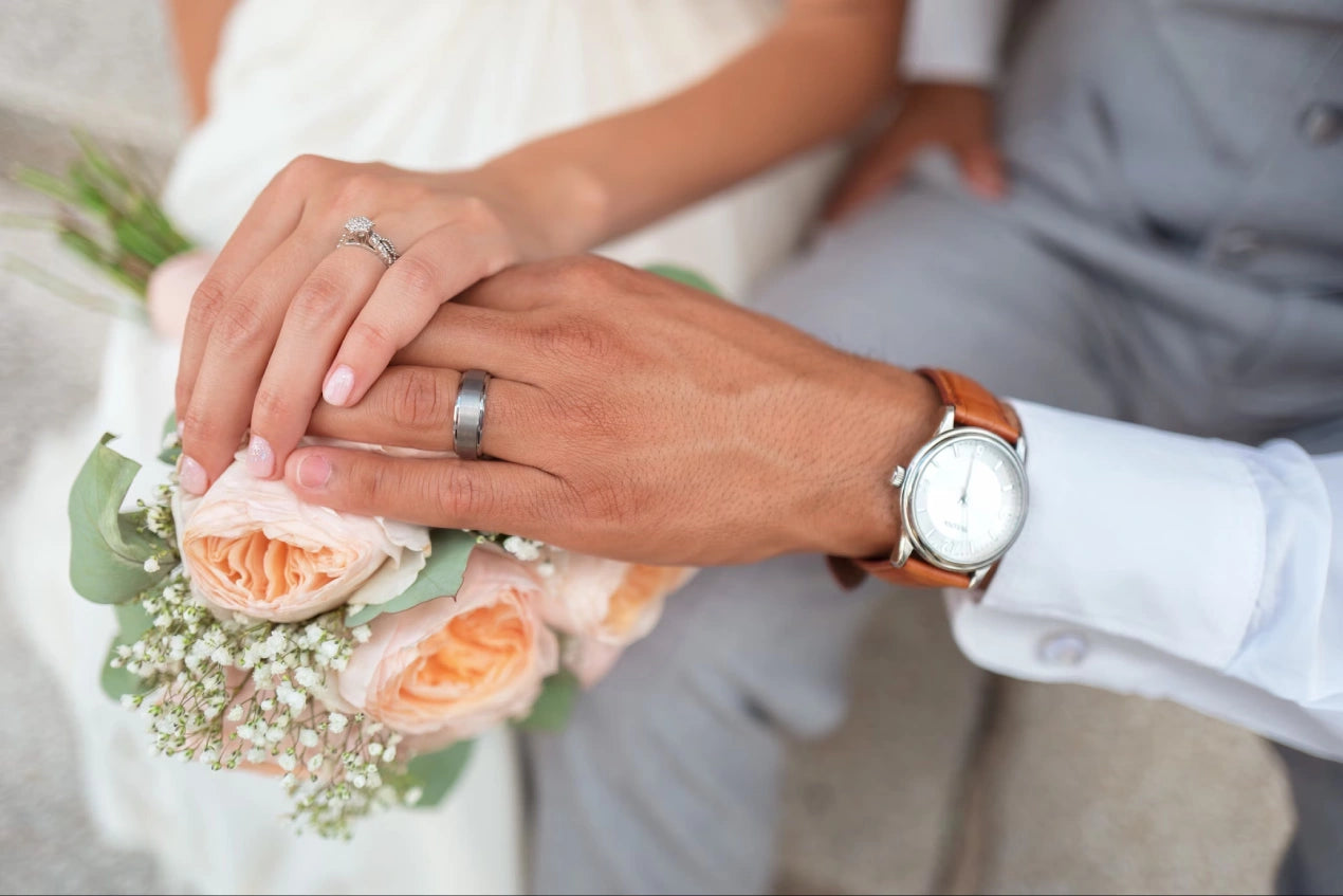 A couple with an engagement rings, holding their hand on a flower bouquet 