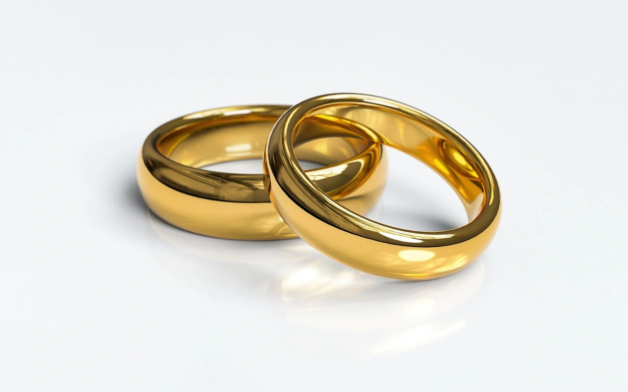 Two golden engagement rings are placed on a white surface