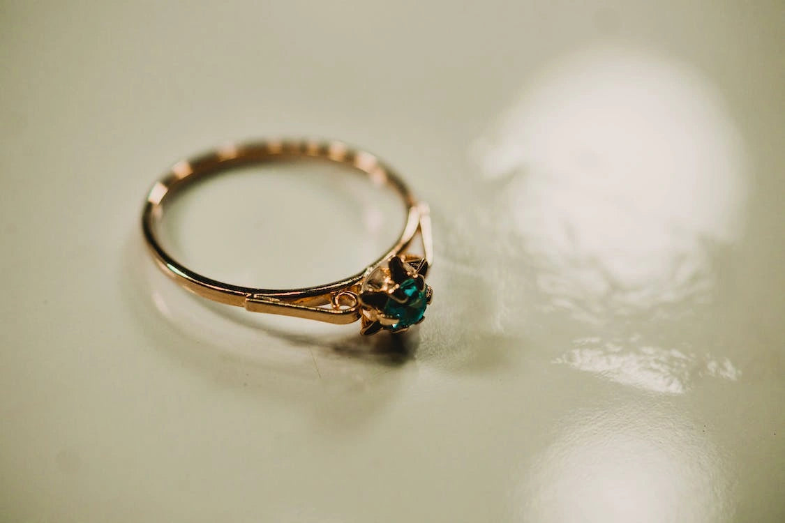 A gold engagement ring with a green stone placed on the surface